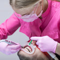 Dental professional in pink coat and gloves performing a dental procedure on a patient.