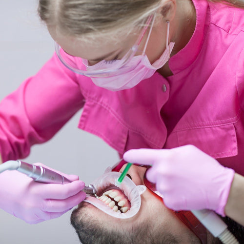 Dental professional in pink coat and gloves performing a dental procedure on a patient.